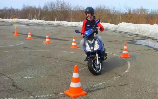 Ученик на мотоцикле выполняет упражнение на площадке автошколы